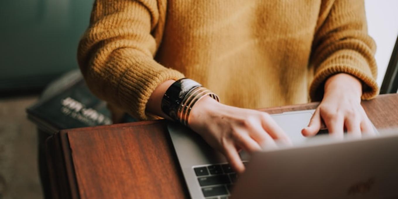 Person typing on a laptop wearing a mustard sweater.